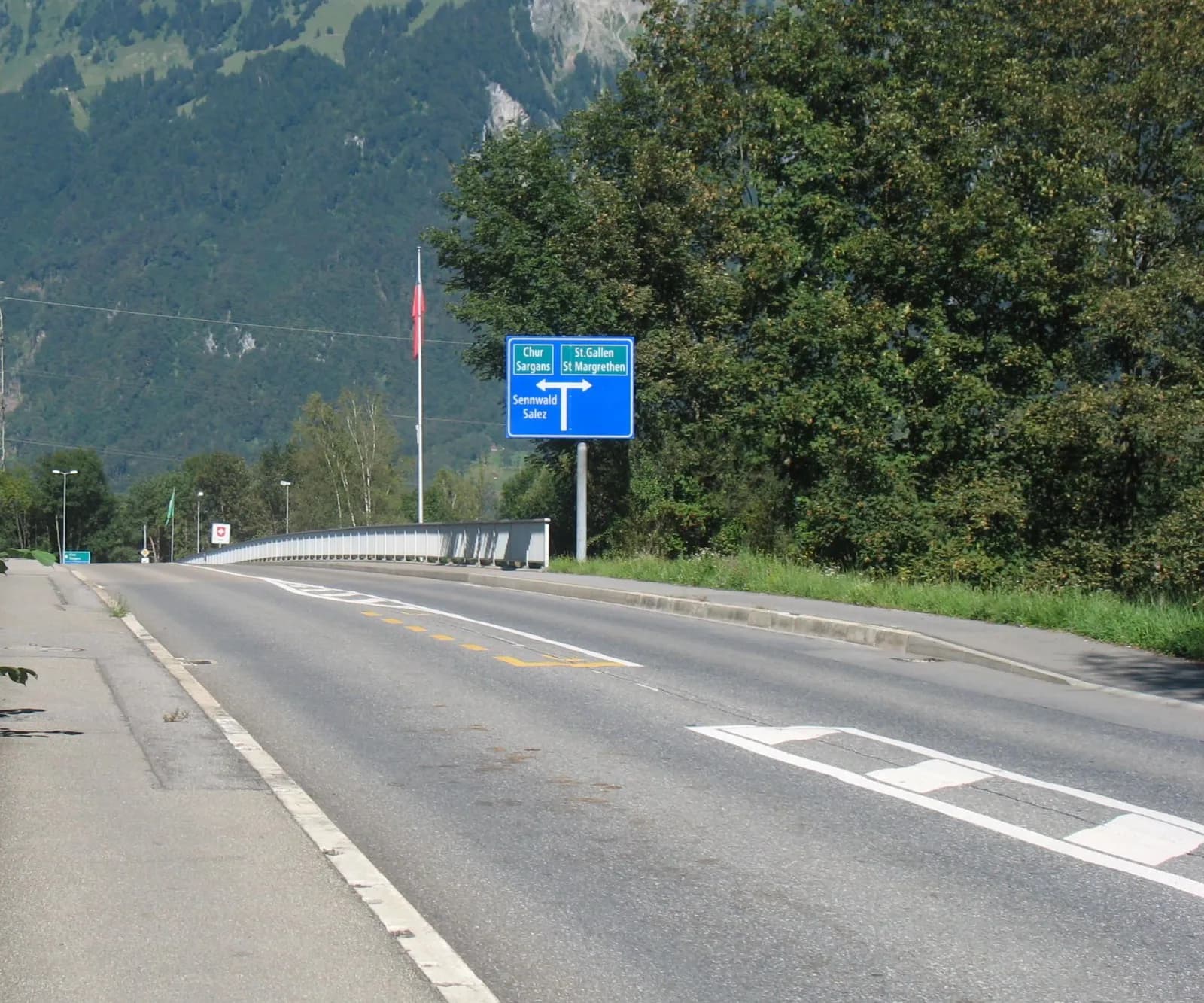 Route vide bordée d'arbres en Suisse orientale, montagnes en arrière-plan