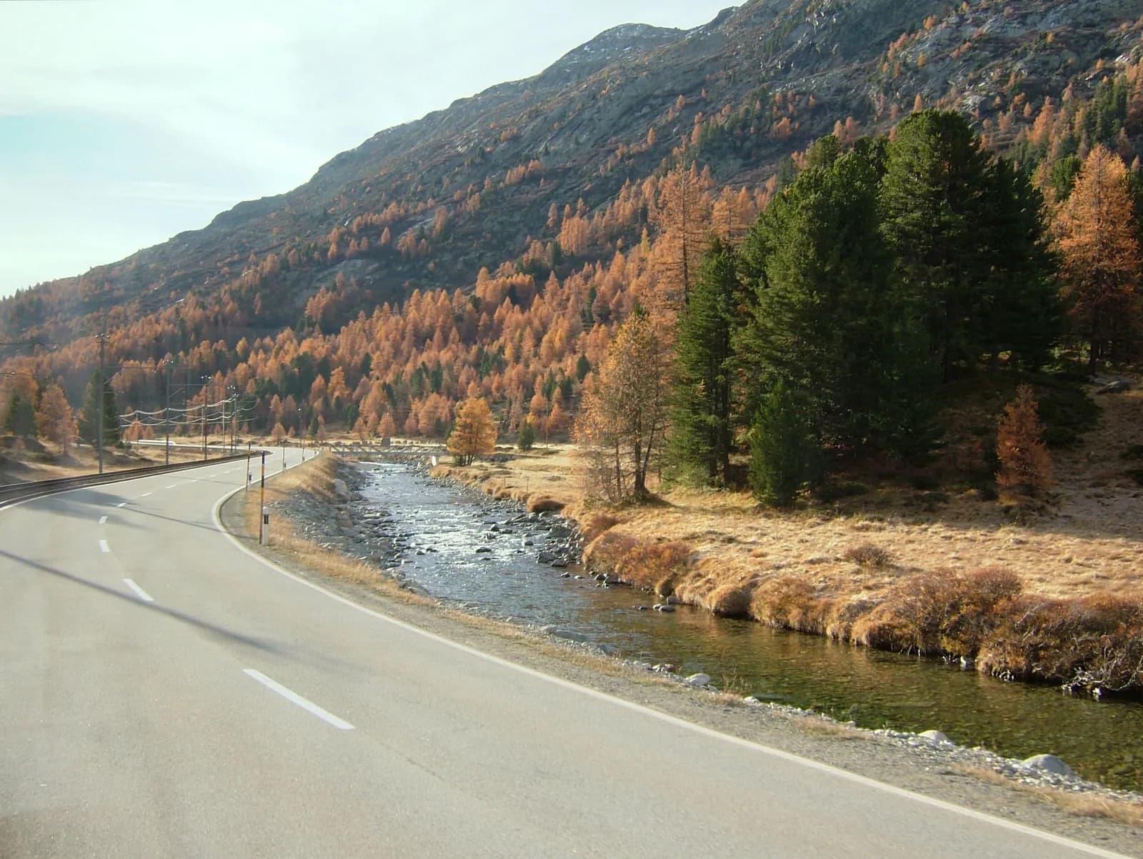 Route de montagne déserte longeant une rivière, mélèzes aux couleurs d'automne